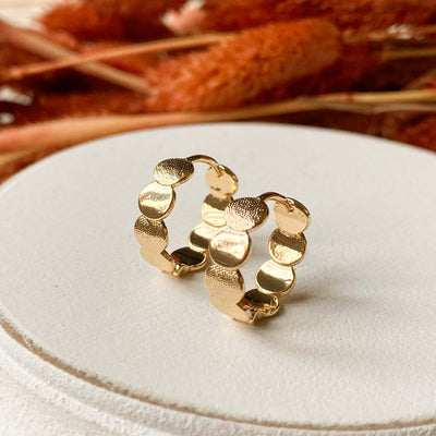 Gold hoop earrings on a white cushion with dried plants in the background