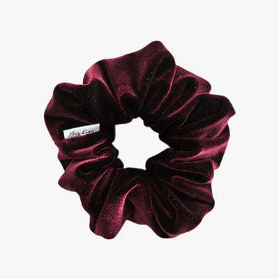Maroon velvet scrunchie with a brand label on a white background
