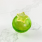 A green, spherical tea bomb topped with a yellow star. The tea bomb is resting on a white marble surface.