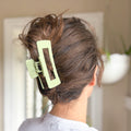 Person with a green hair clip in their hair, standing in front of a mirror.