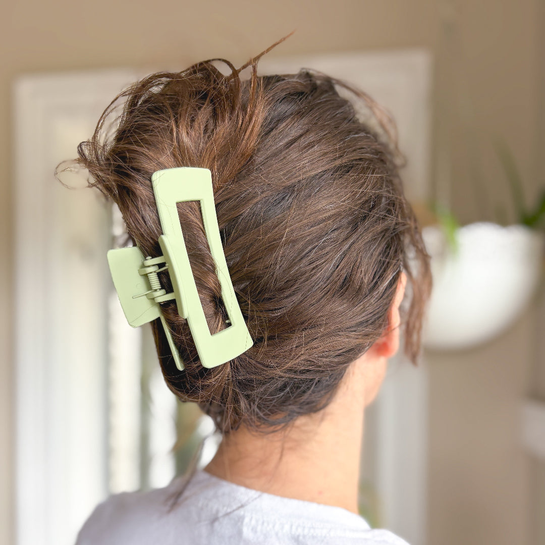 Person with a green hair clip in their hair, standing in front of a mirror.