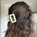 Close-up of wavy hair with a green hair clip against a blurred background