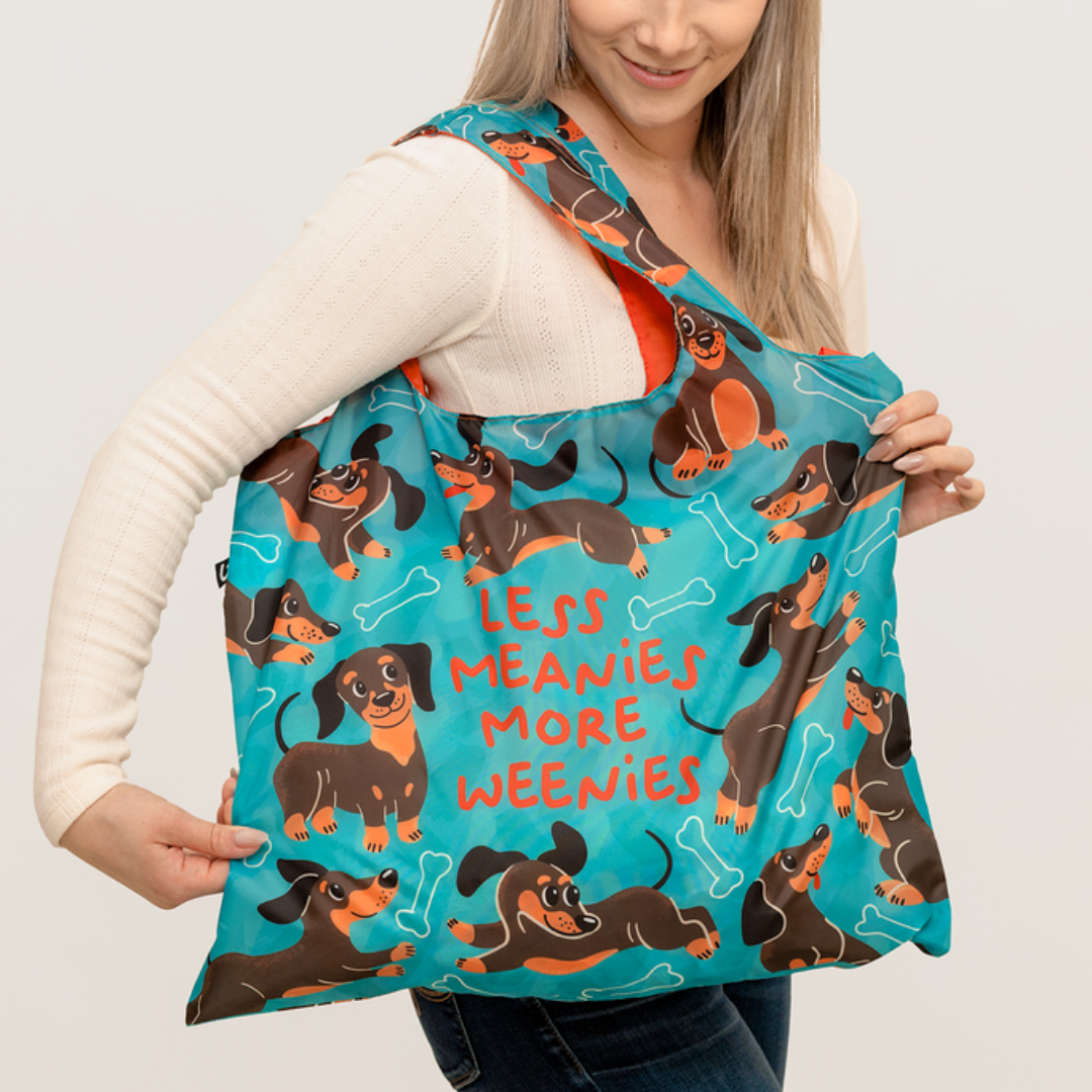 Woman holding a teal bag with dachshund illustrations and text.