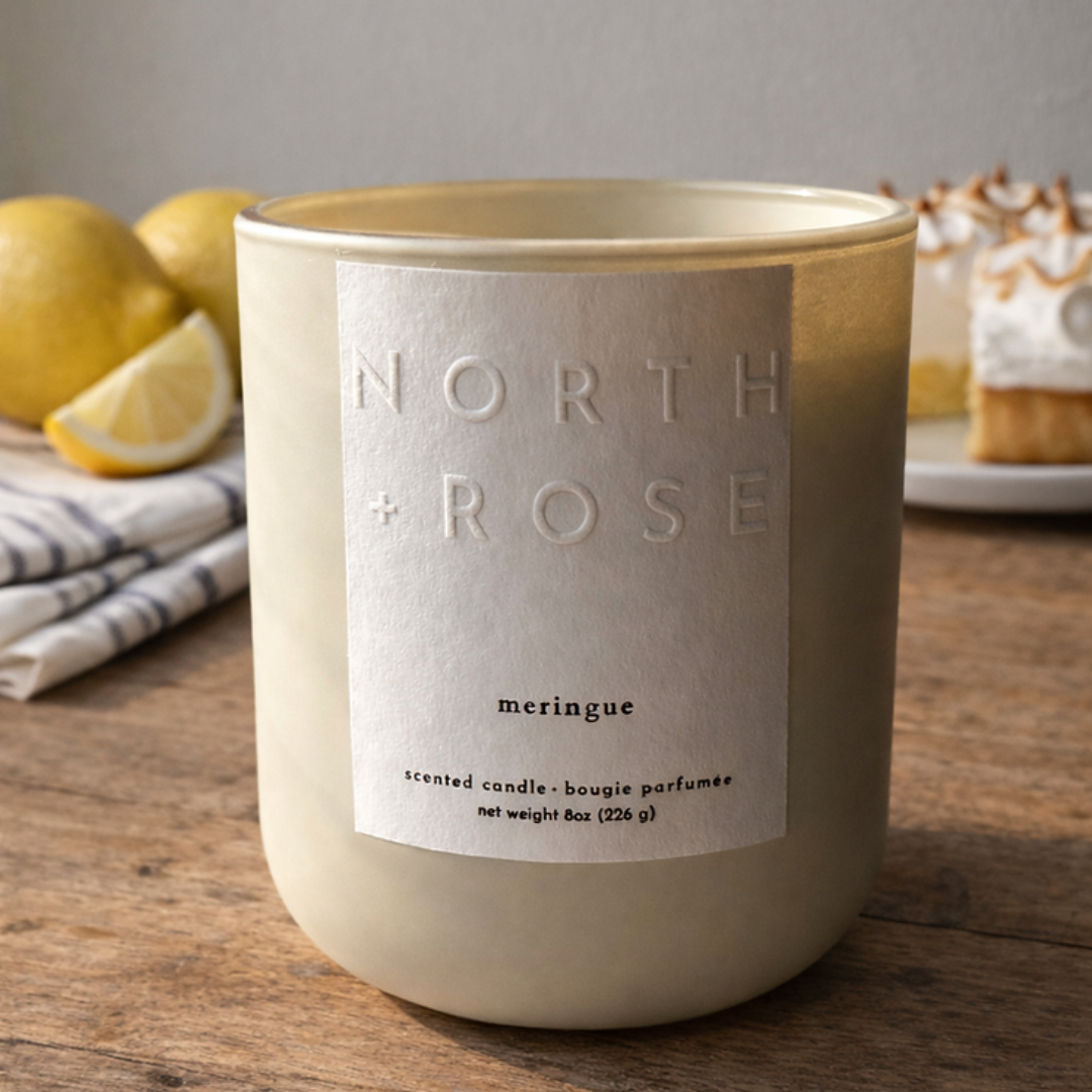Candle labeled 'North + Rose' on a wooden surface with lemons and pastries in the background.