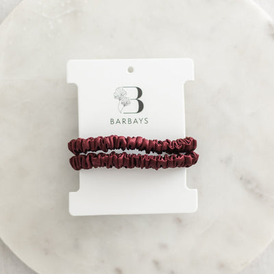 Two burgundy hair ties on a white Barbays branded card against a marble background