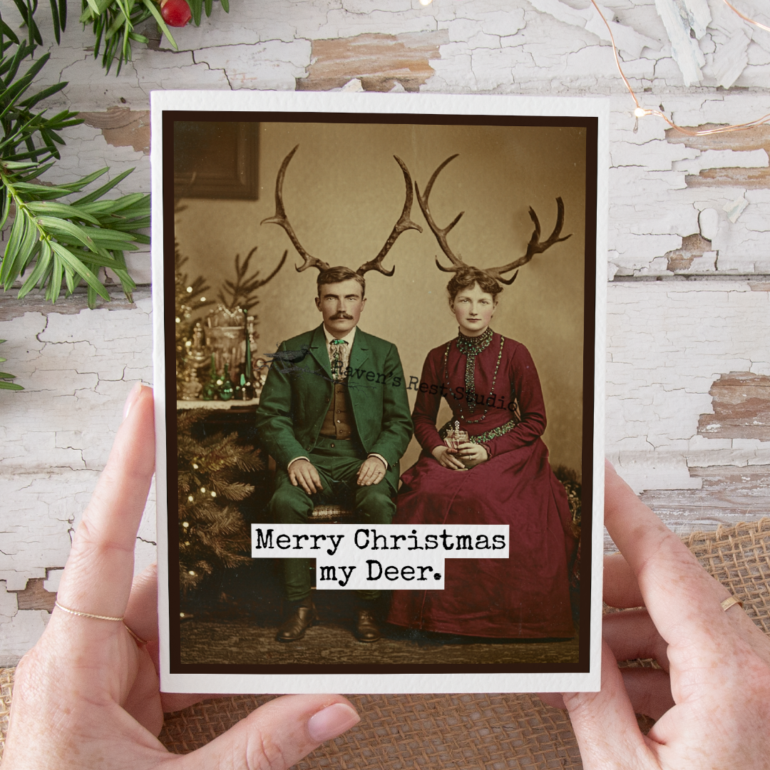 Vintage-style Christmas card with a couple wearing antlers and text 'Merry Christmas my Deer' held by hands.