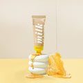 Tube of milk and honey product with honey being dripped onto a stack of white cookies on a beige background.