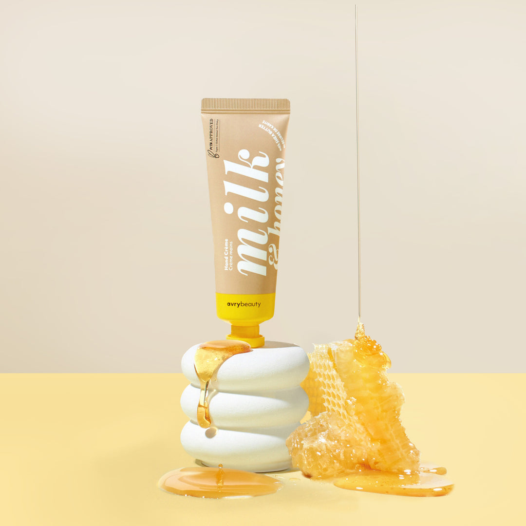 Tube of milk and honey product with honey being dripped onto a stack of white cookies on a beige background.