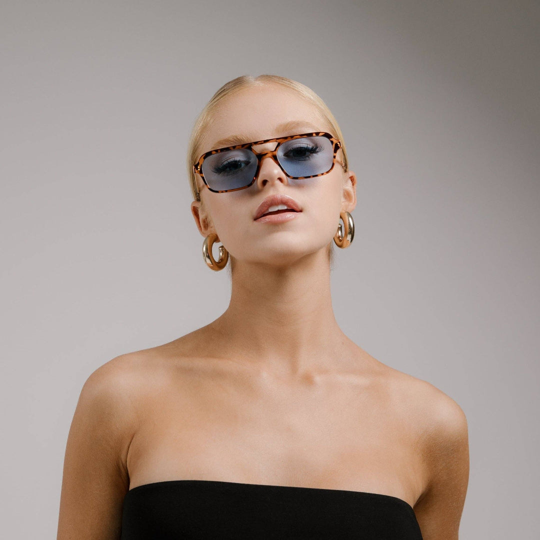 Woman wearing sunglasses and hoop earrings against a plain background