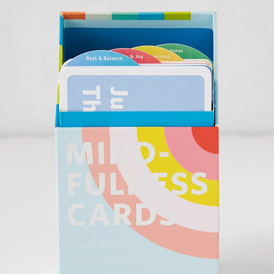 A boxed deck of 'Mindfulness Cards' standing upright on a light gray background. The packaging is light blue with large white text and abstract curved shapes in coral, yellow, and pink.