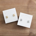 Two pairs of bee-shaped earrings on Birch Jewellery cards on a wooden surface.