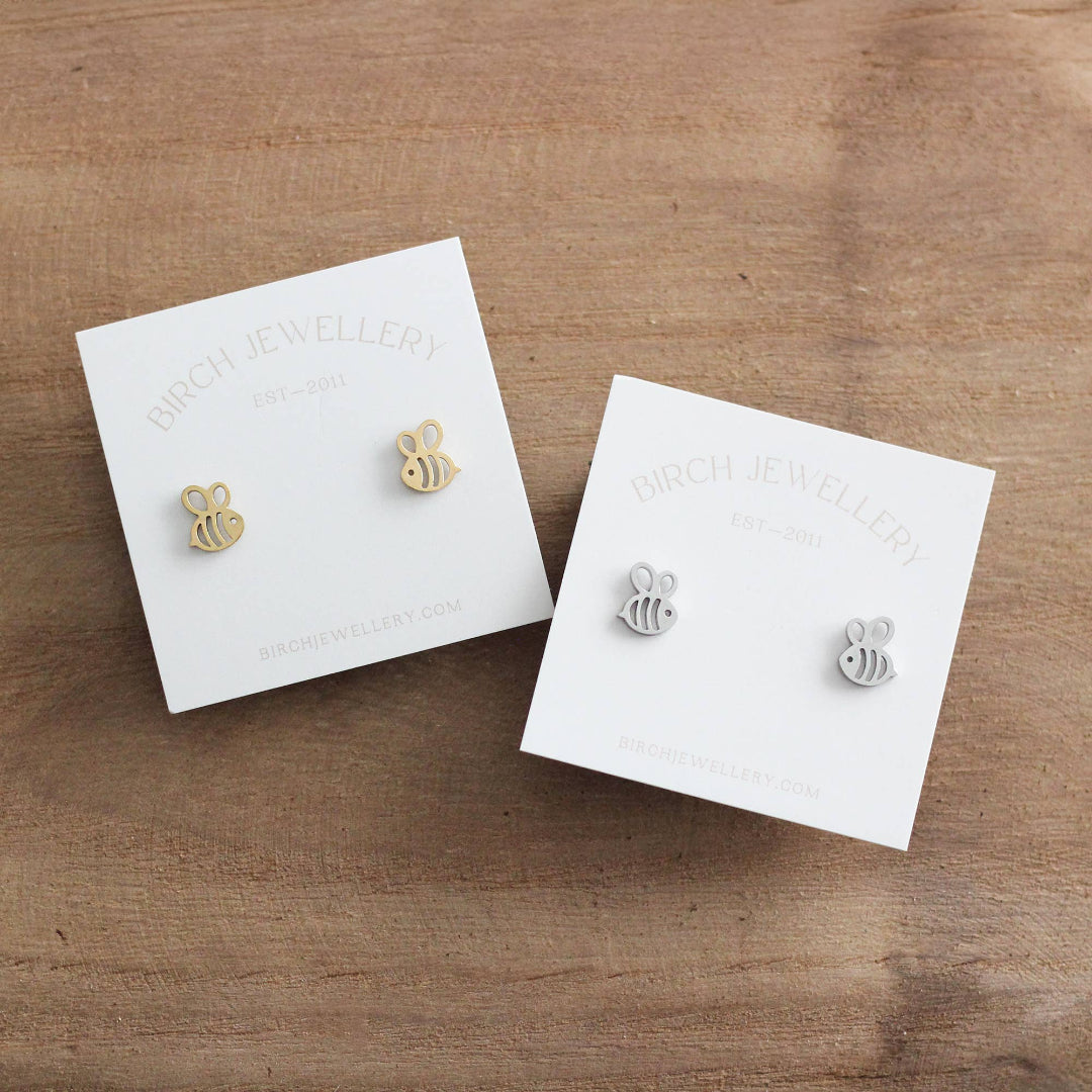 Two pairs of bee-shaped earrings on Birch Jewellery cards on a wooden surface.