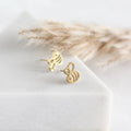 Gold bee-shaped earrings on a white surface with dried plants in the background