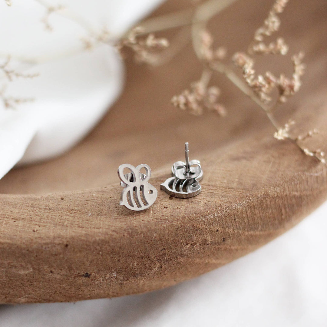 Silver bee-shaped earrings on a wooden surface with a white background