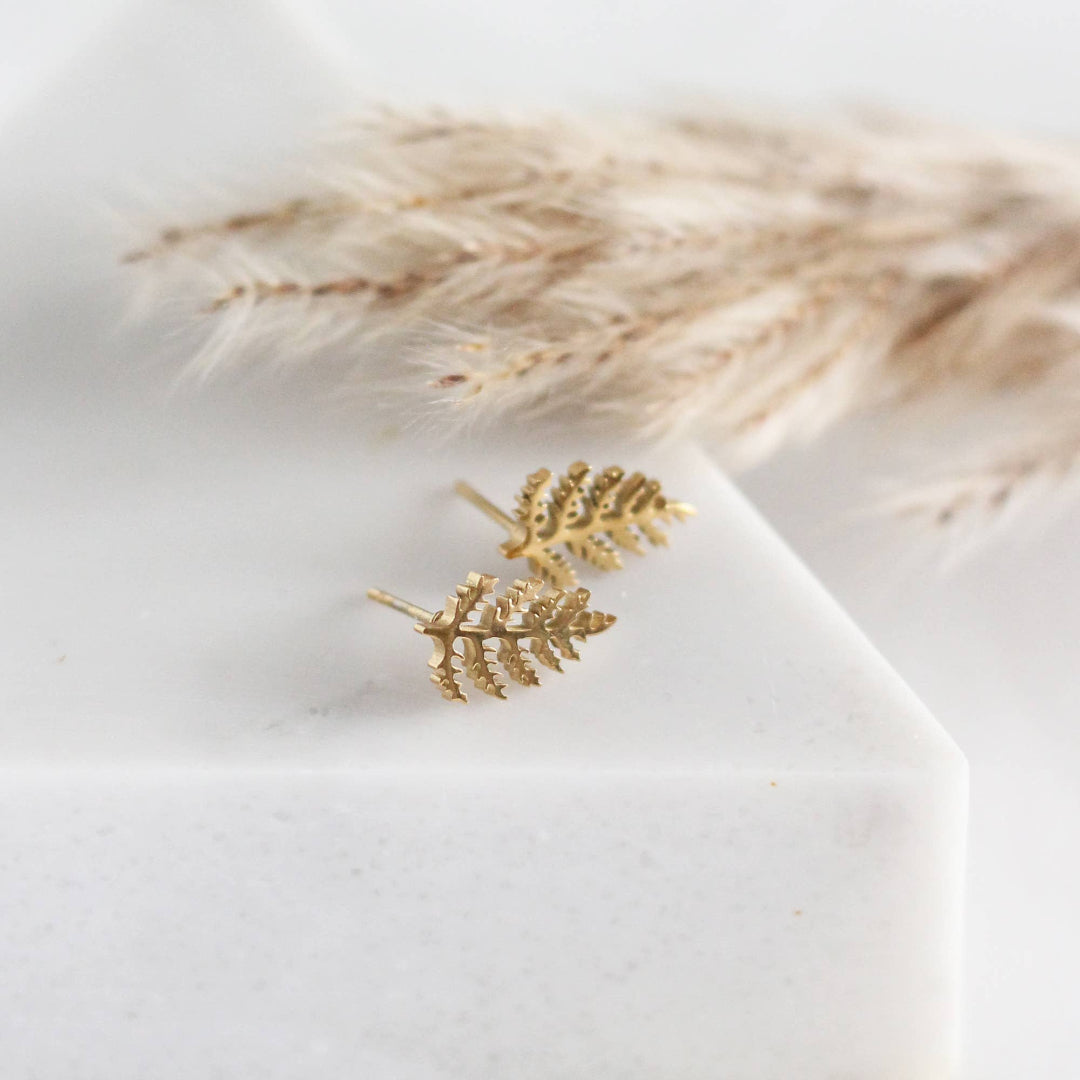Gold leaf earrings on a white surface with dried pampas grass in the background