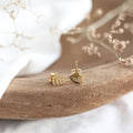 Gold leaf earrings on a wooden surface with a blurred natural background