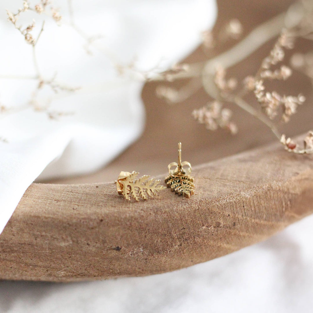 Gold leaf earrings on a wooden surface with a blurred natural background