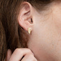 Close-up of a person wearing a gold leaf-shaped earring.