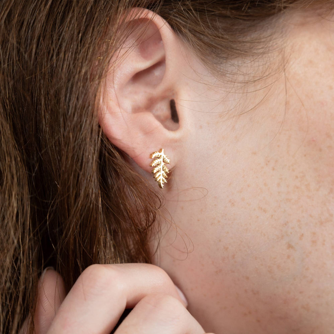 Close-up of a person wearing a gold leaf-shaped earring.