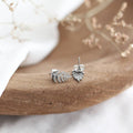 Silver leaf-shaped earrings on a wooden surface with a blurred natural background
