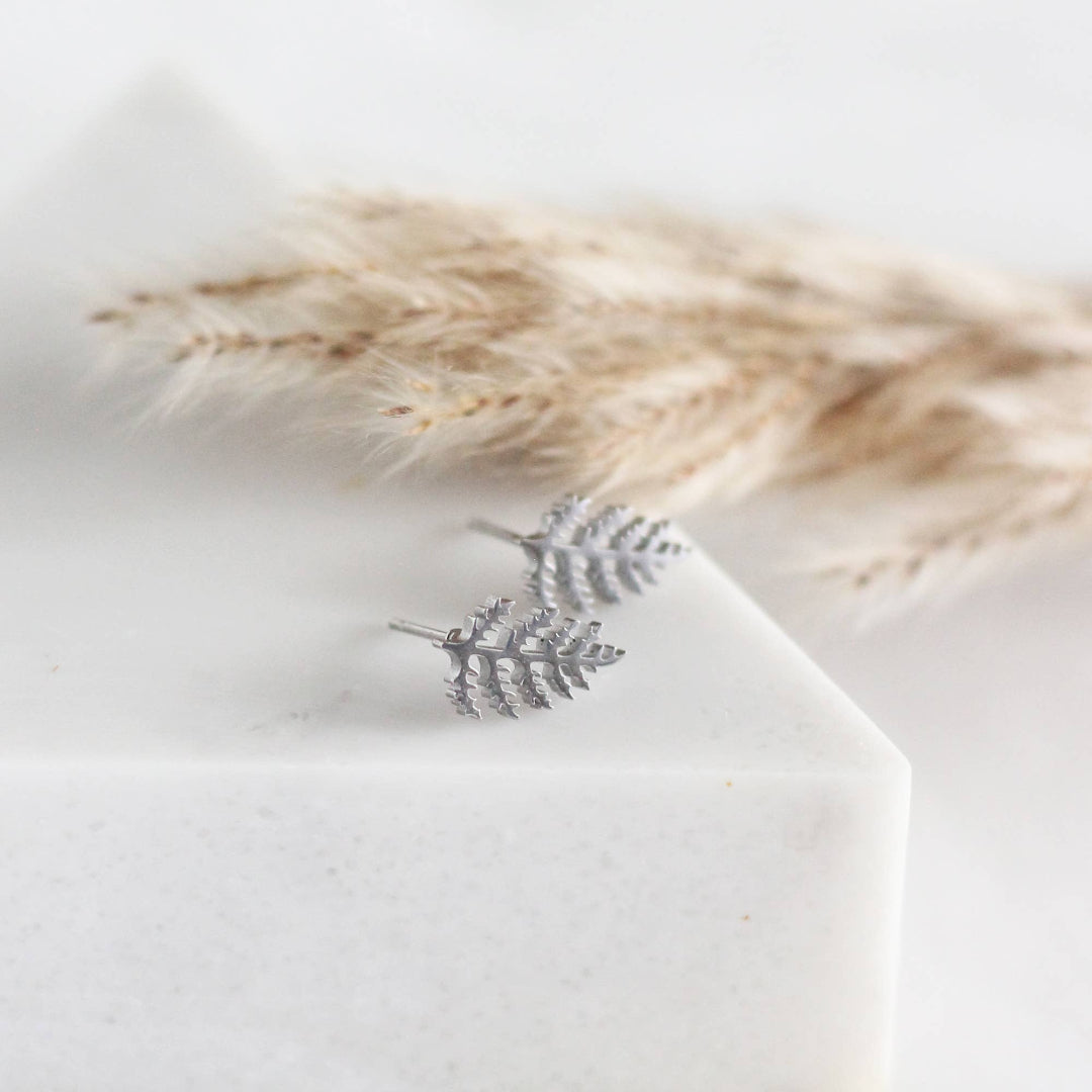Silver leaf earring on a white surface with dried pampas grass in the background