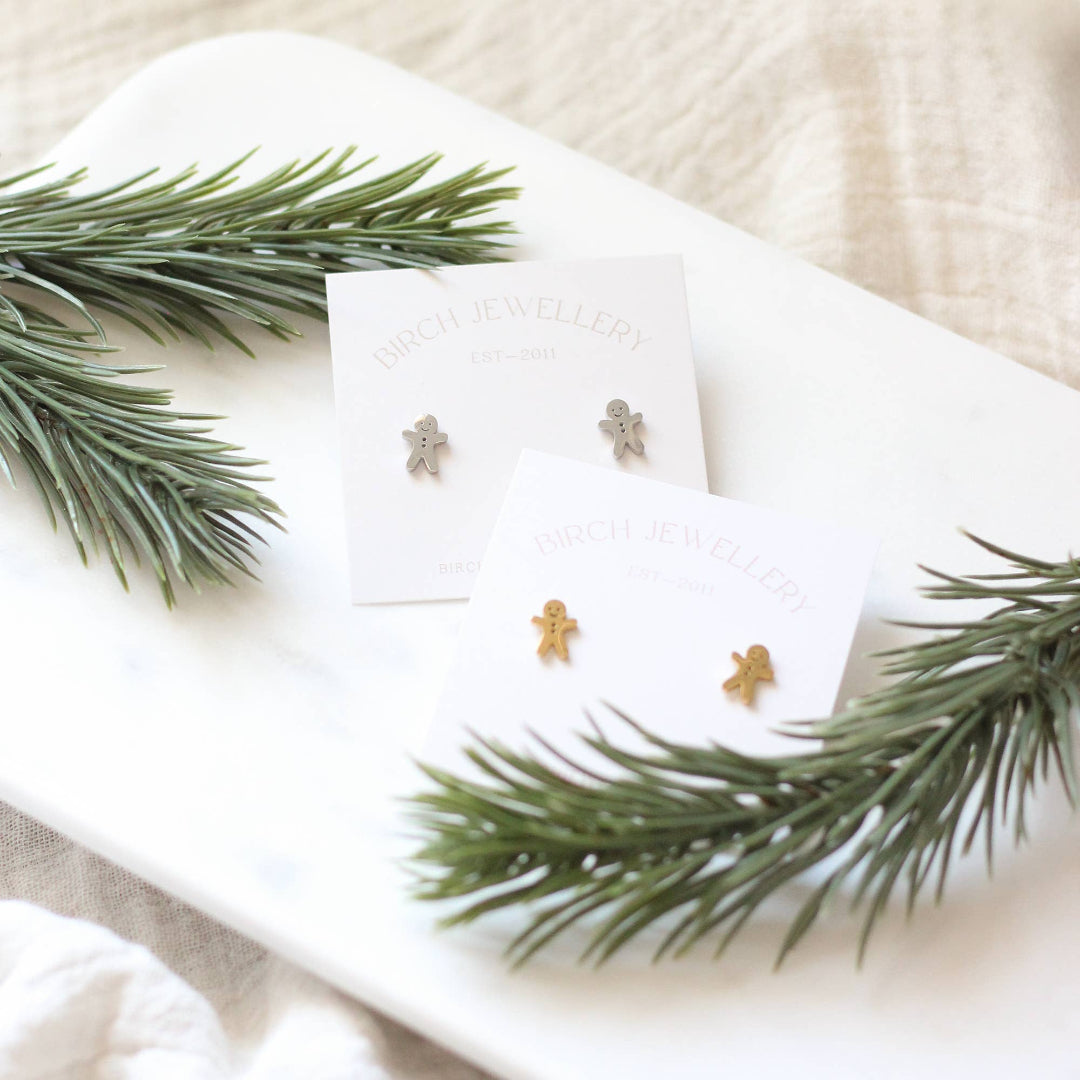 Gold gingerbread man earrings on a white card with greenery