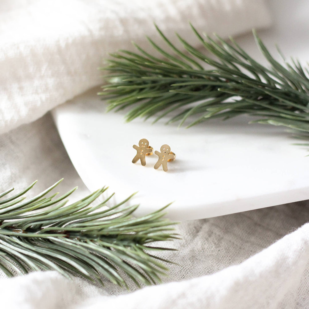 Gold gingerbread man earrings on a white dish with greenery
