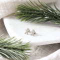 Silver gingerbread man earrings on a white plate with greenery