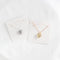 Two heart-shaped locket necklaces on a white card. One necklace has a gold-colored locket, and the other has a silver-colored locket. Both lockets have detailed designs and are attached to delicate chains.