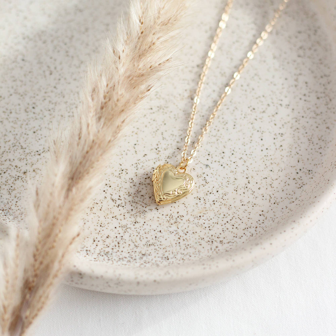 Gold heart-shaped necklace on a textured surface with dried pampas grass
