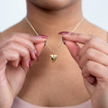Gold heart-shaped necklace being held by a person with a blurred background