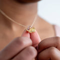Gold heart-shaped necklace held by a hand against a blurred background