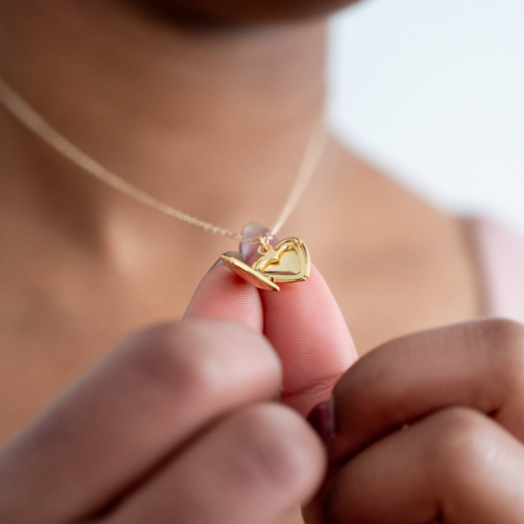 Gold heart-shaped necklace held by a hand against a blurred background