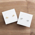 Gold and silver bee-shaped earrings on branded cards on a wooden surface