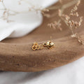 Gold bee-shaped earrings on a wooden surface with a blurred background