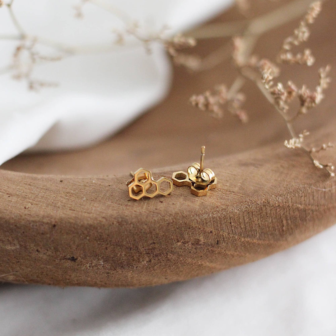 Gold bee-shaped earrings on a wooden surface with a blurred background