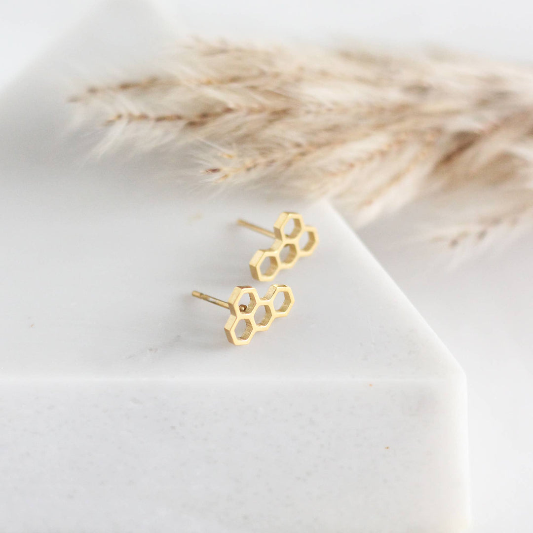 Gold honeycomb earrings on a white surface with dried grass in the background