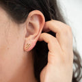 Close-up of a person wearing a gold earring with a hand adjusting it.