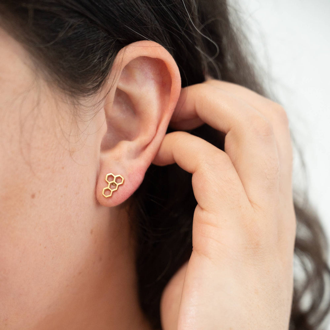 Close-up of a person wearing a gold earring with a hand adjusting it.