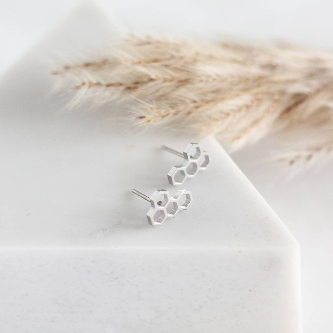 Silver honeycomb earrings on a white surface with dried grasses in the background