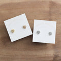 Two pairs of maple leaf shaped earrings on white cards with 'Birch & Willow' branding on a wooden surface.