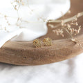 Gold leaf-shaped earrings on a wooden surface with a white background