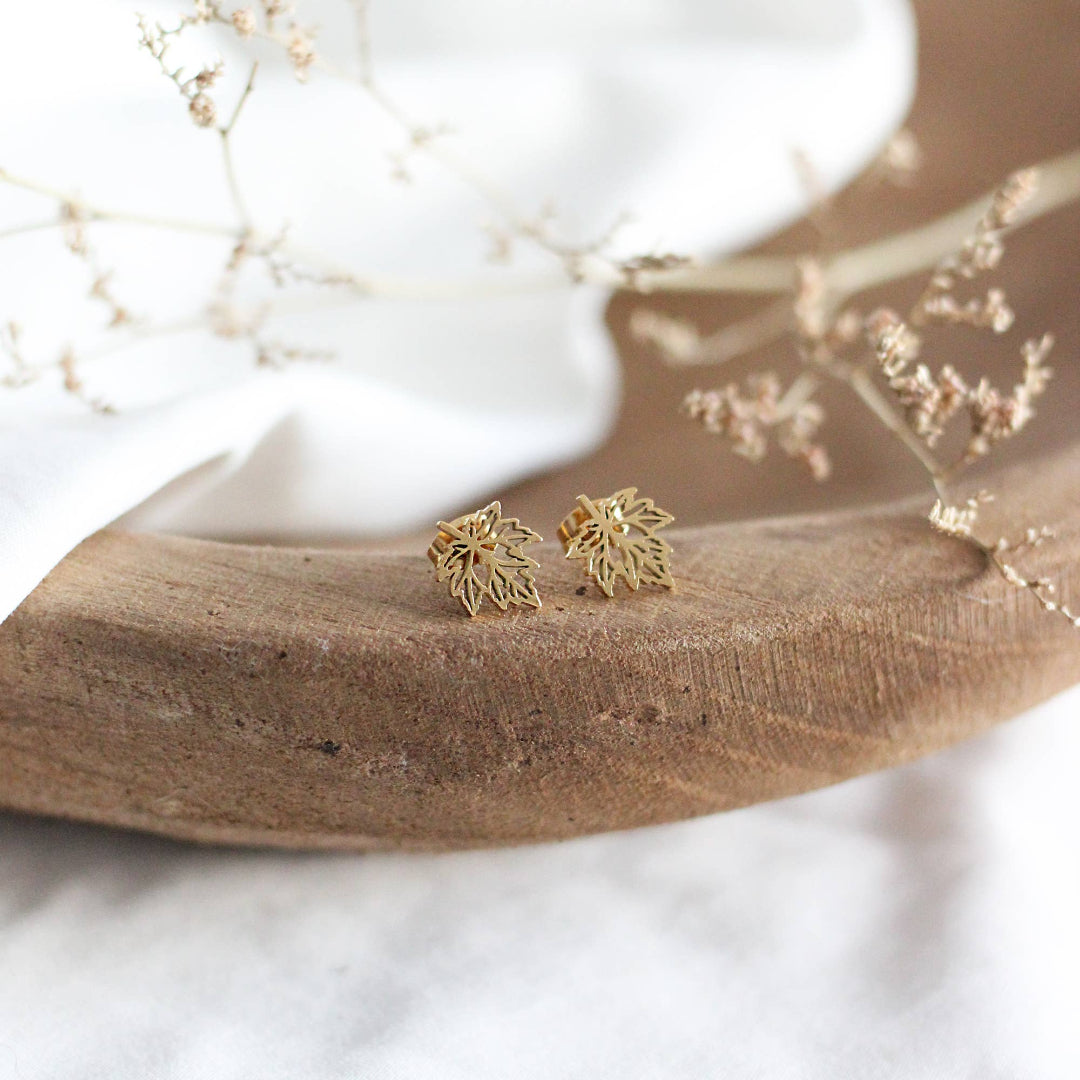 Gold leaf-shaped earrings on a wooden surface with a white background