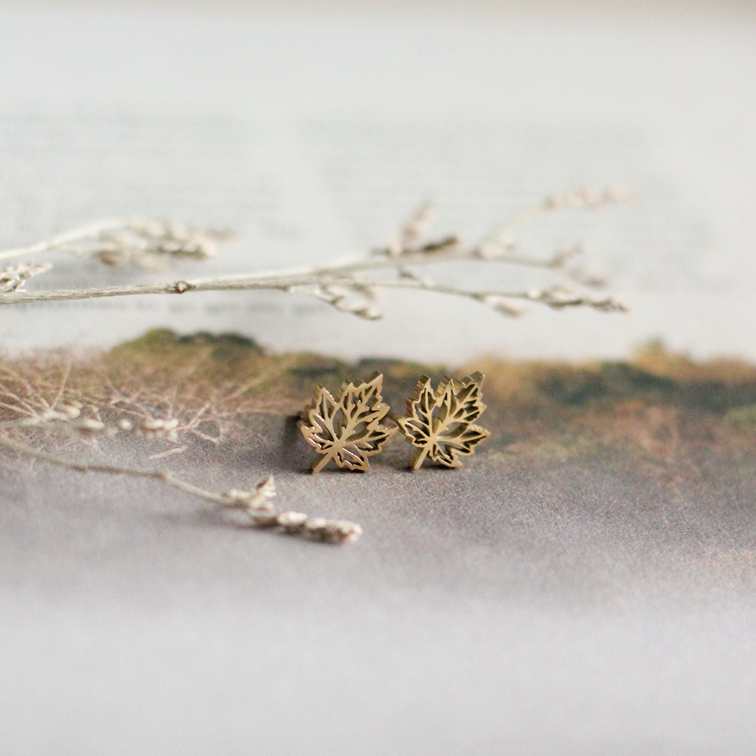 Gold leaf-shaped earrings on a reflective surface with a natural background