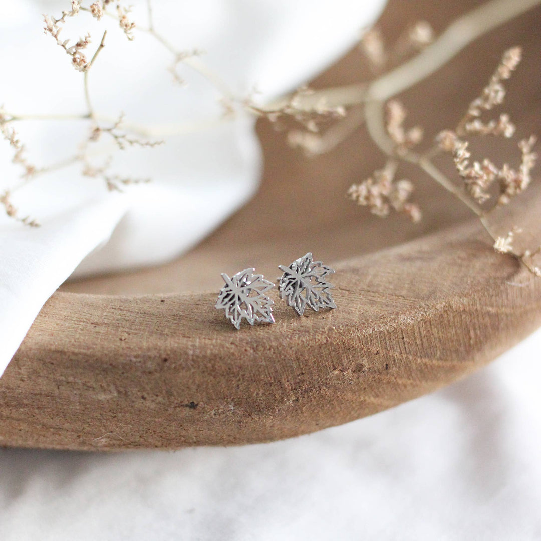 Silver leaf-shaped earrings on a wooden surface with a blurred natural background