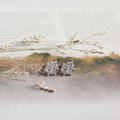 Silver leaf-shaped earrings on a light background with dried branches.
