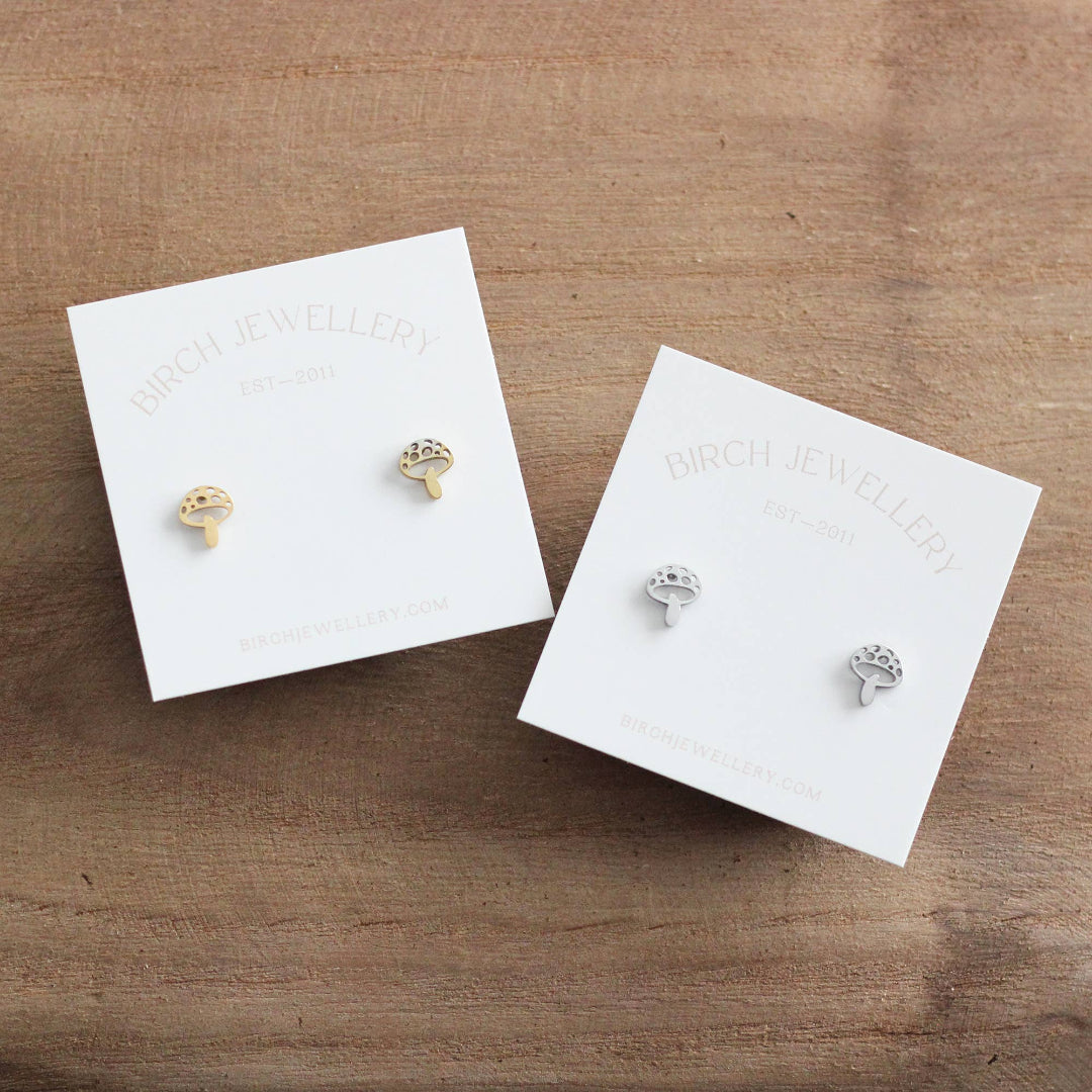 Two pairs of earrings on branded card holders on a wooden surface