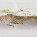 Gold leaf-shaped earrings on a neutral background with dried branches.
