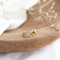 Gold mushroom-shaped earrings on a natural wood surface with a blurred background