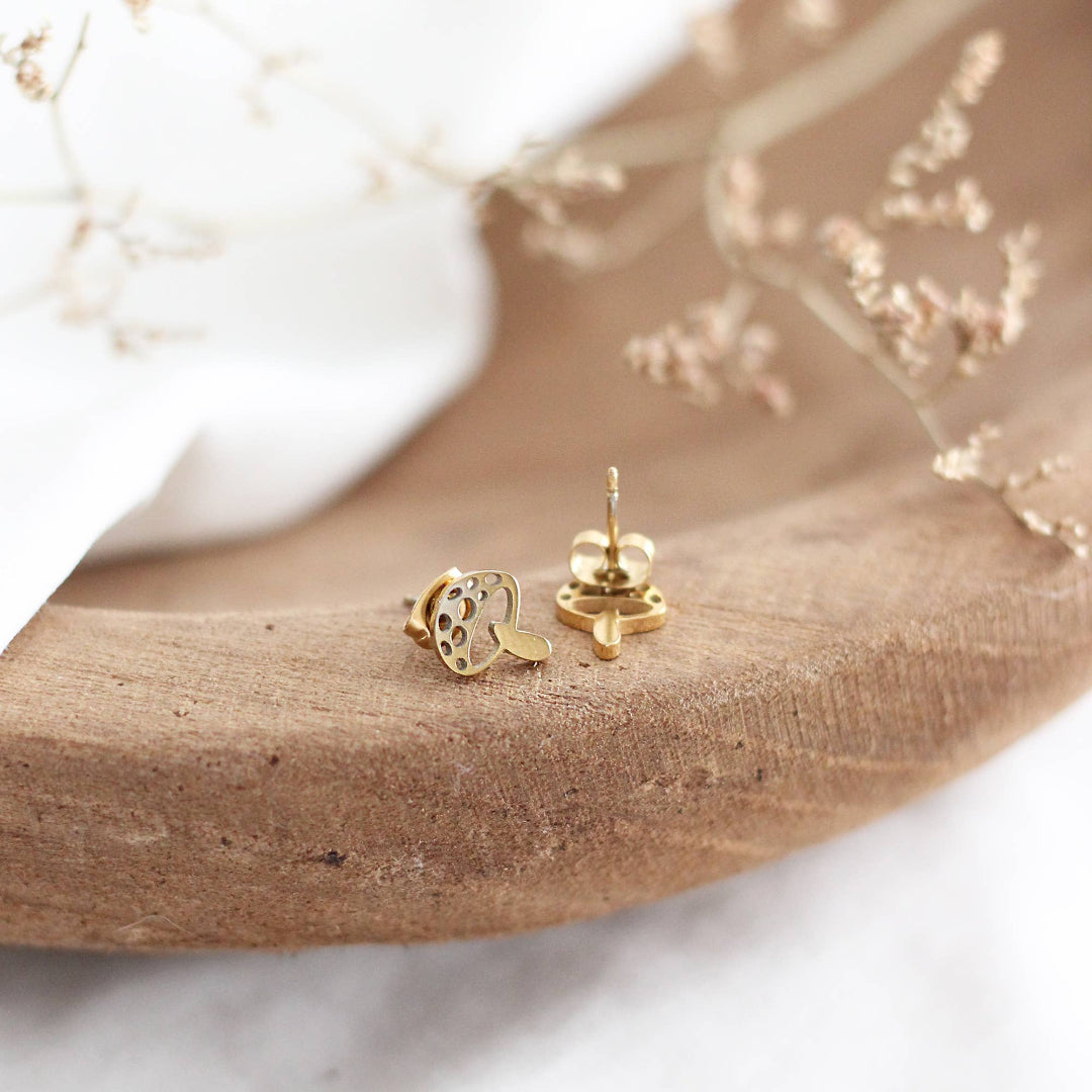 Gold mushroom-shaped earrings on a natural wood surface with a blurred background